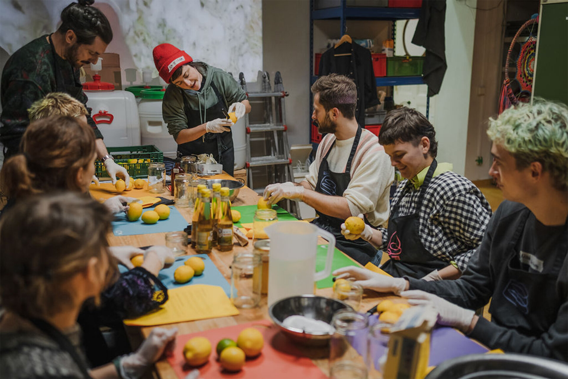 Workshopsituation: Mehrere Menschen in Kochschürzen sitzen zusammen am Tisch und bereiten Essen mit Zitronen zu.