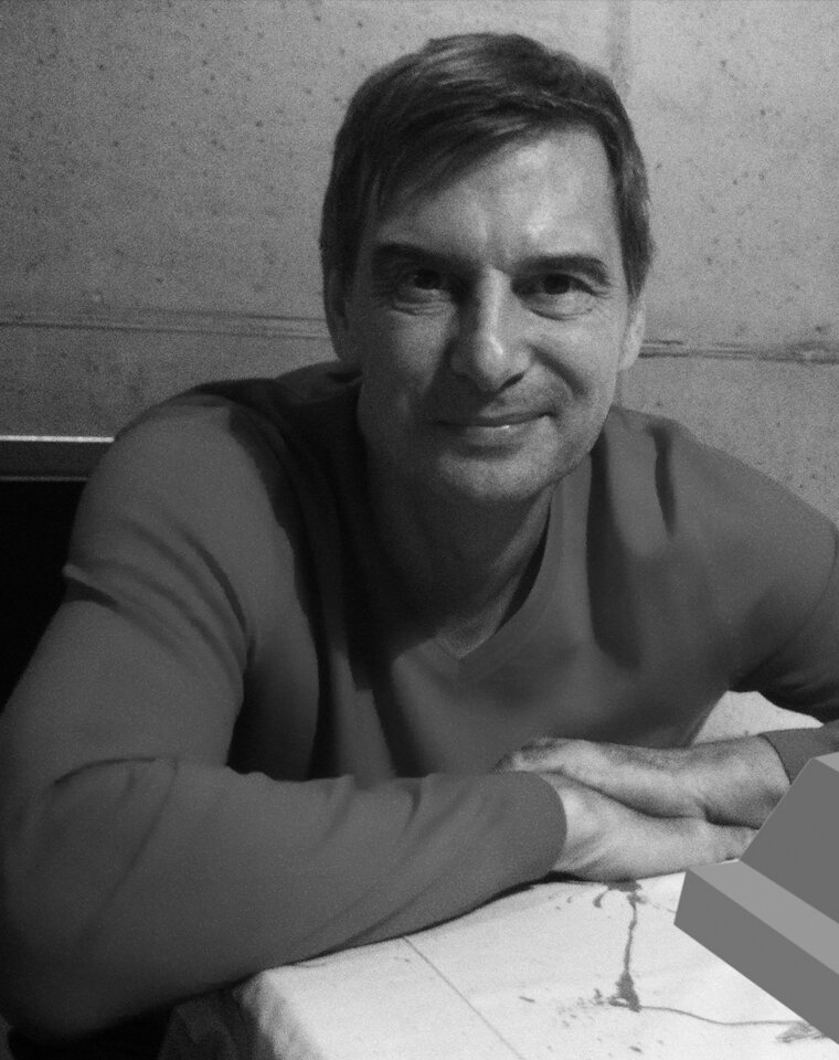 schwarz-weiss Portrait des vor einer Betonwand sitzenden Architekten Harald Schindele