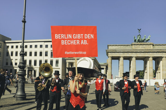 Gruppe von Menschen, festlich gekleidet, hält ein Schild hoch und steht vor dem Brandenburger Tor in Berlin